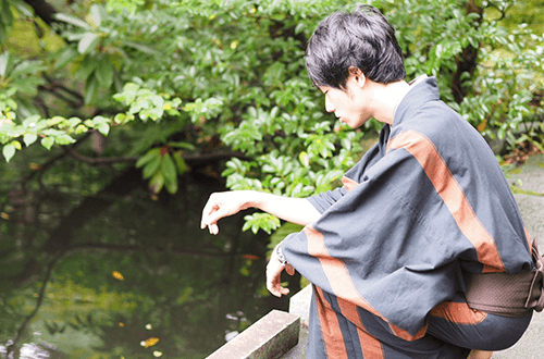 着物姿で池をのぞき込む圓尾和紀さんの写真